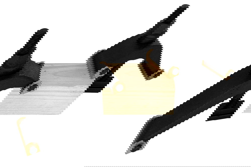 Black hold-downs with gold Two black hold-downs with gold accents hold a light-coloured piece of wood in place. Each hold-down has a screw to adjust the pressure.